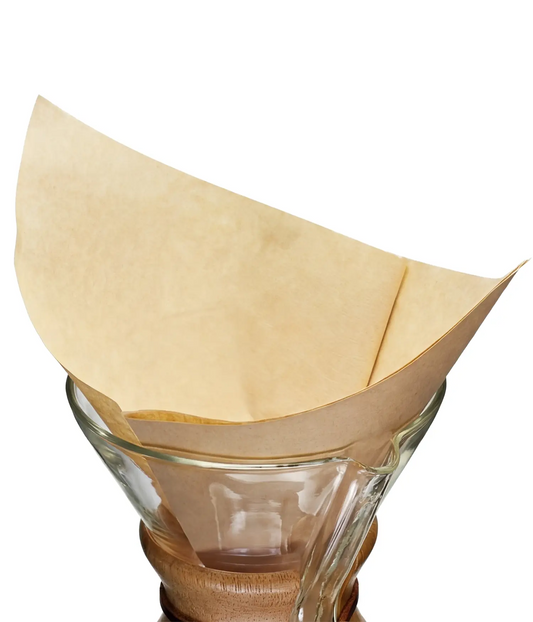 A natural brown 30x30cm flat square coffee filter, folded into a cone, sitting inside a classic glass pour-over coffee maker.