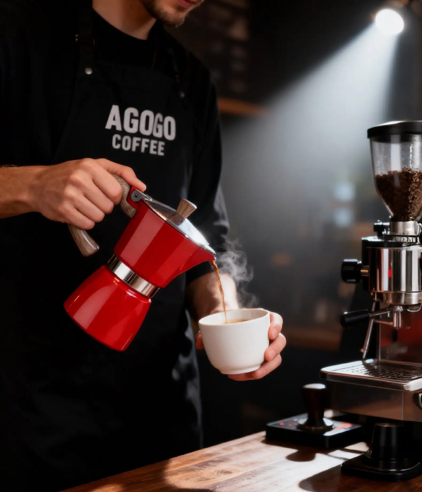 A professional barista wearing an AGOGO Coffee apron pouring fresh espresso from the vintage red Milano Moka Pot into a white cup in a moody, atmospheric cafe.