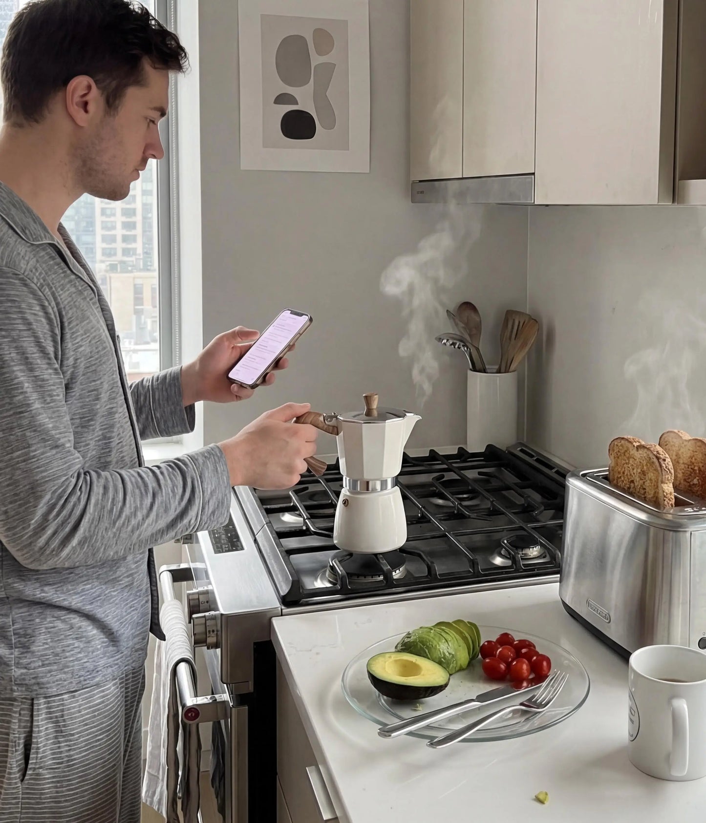 A man checking his phone in a modern kitchen while brewing his morning espresso with the warm cream AGOGO Moka Pot on a gas stove next to a toaster.