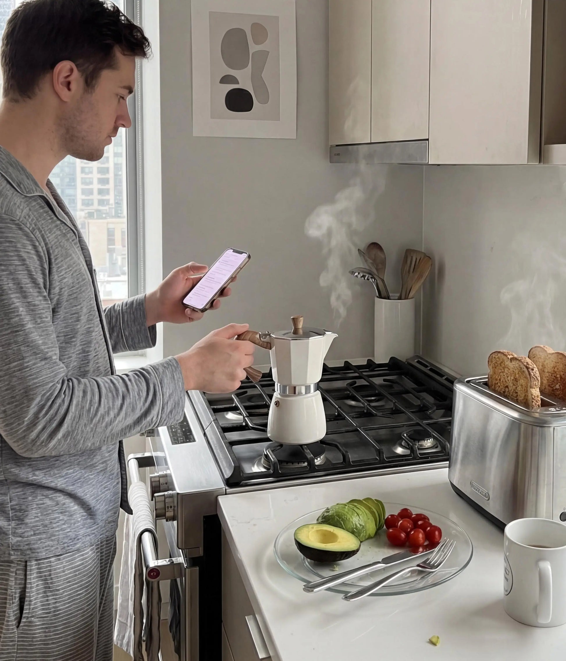 A man checking his phone in a modern kitchen while brewing his morning espresso with the warm cream AGOGO Moka Pot on a gas stove next to a toaster.
