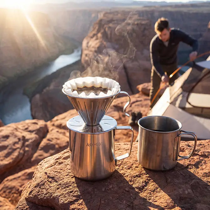 Steaming hot coffee brewing in an AGOGO rugged stainless steel pour-over dripper and server set, resting on a rocky cliff during a sunny canyon camping trip.