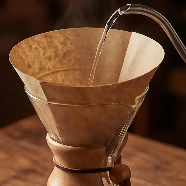 Hands gently placing a natural brown, pre-folded half-moon circle coffee filter seamlessly into a classic glass pour-over brewer.