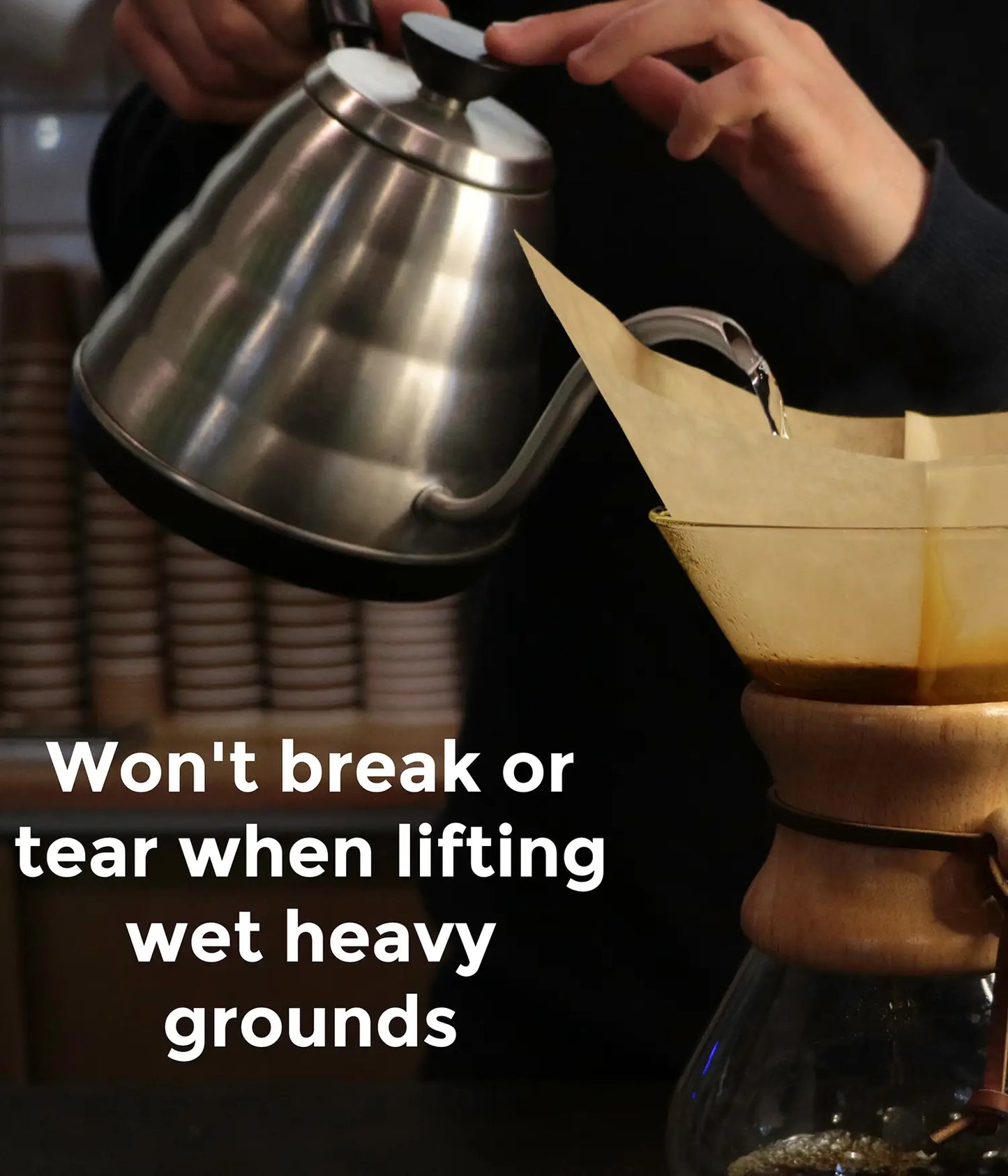A barista pouring hot water from a gooseneck kettle into an AGOGO natural brown coffee filter, demonstrating its 30% thicker, tear-resistant design.